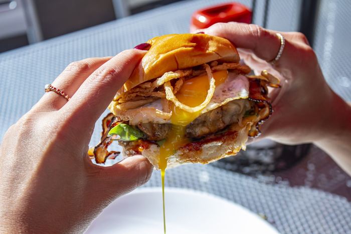 A burger with a runny egg, held over the plate