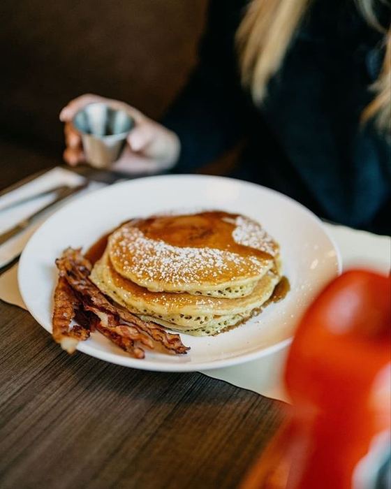 A stack of pancakes with bacon and syrup