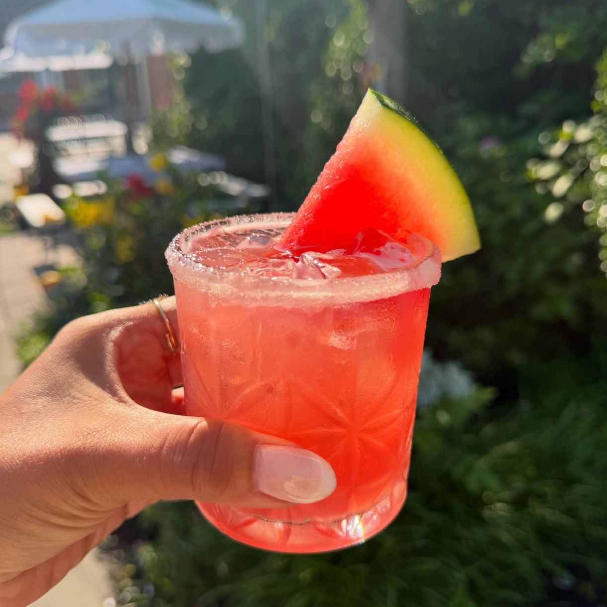A watermelon margarita with a salted rim, held up in the courtyard